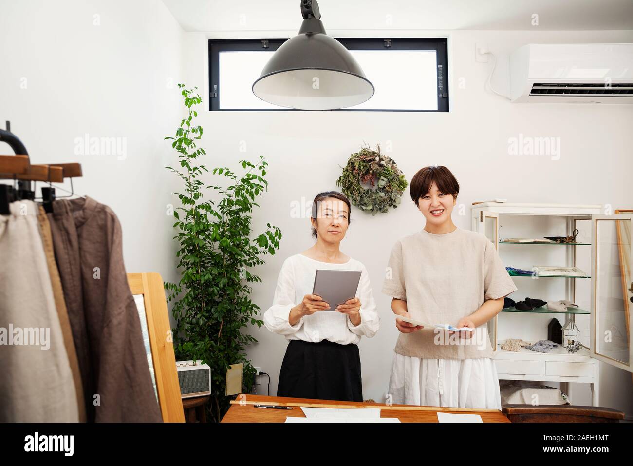 Two Japanese women standing in a small fashion boutique, holding digital tablet, smiling at camera. Stock Photo