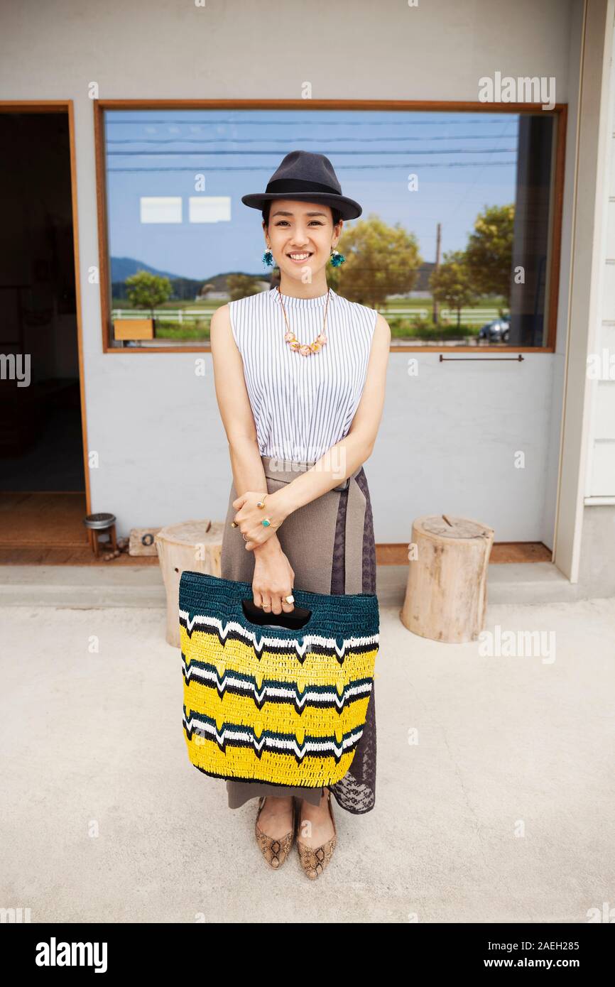 Portrait of smiling Japanese woman wearing hat and holding shopping bag, looking at camera. Stock Photo