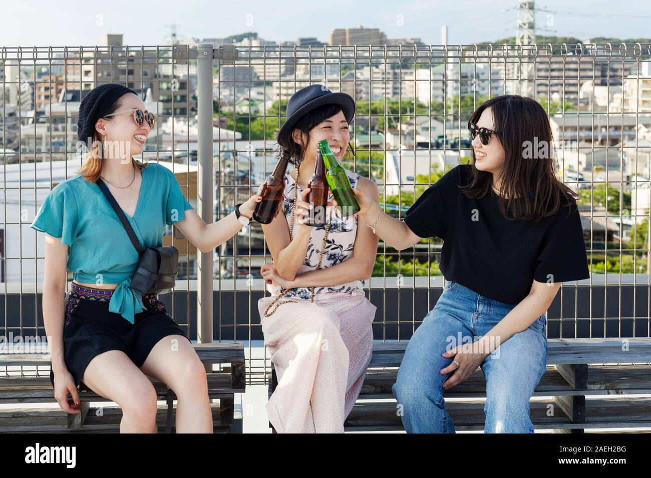 Three young Japanese women sitting on a rooftop in an urban setting, drinking beer. Stock Photo