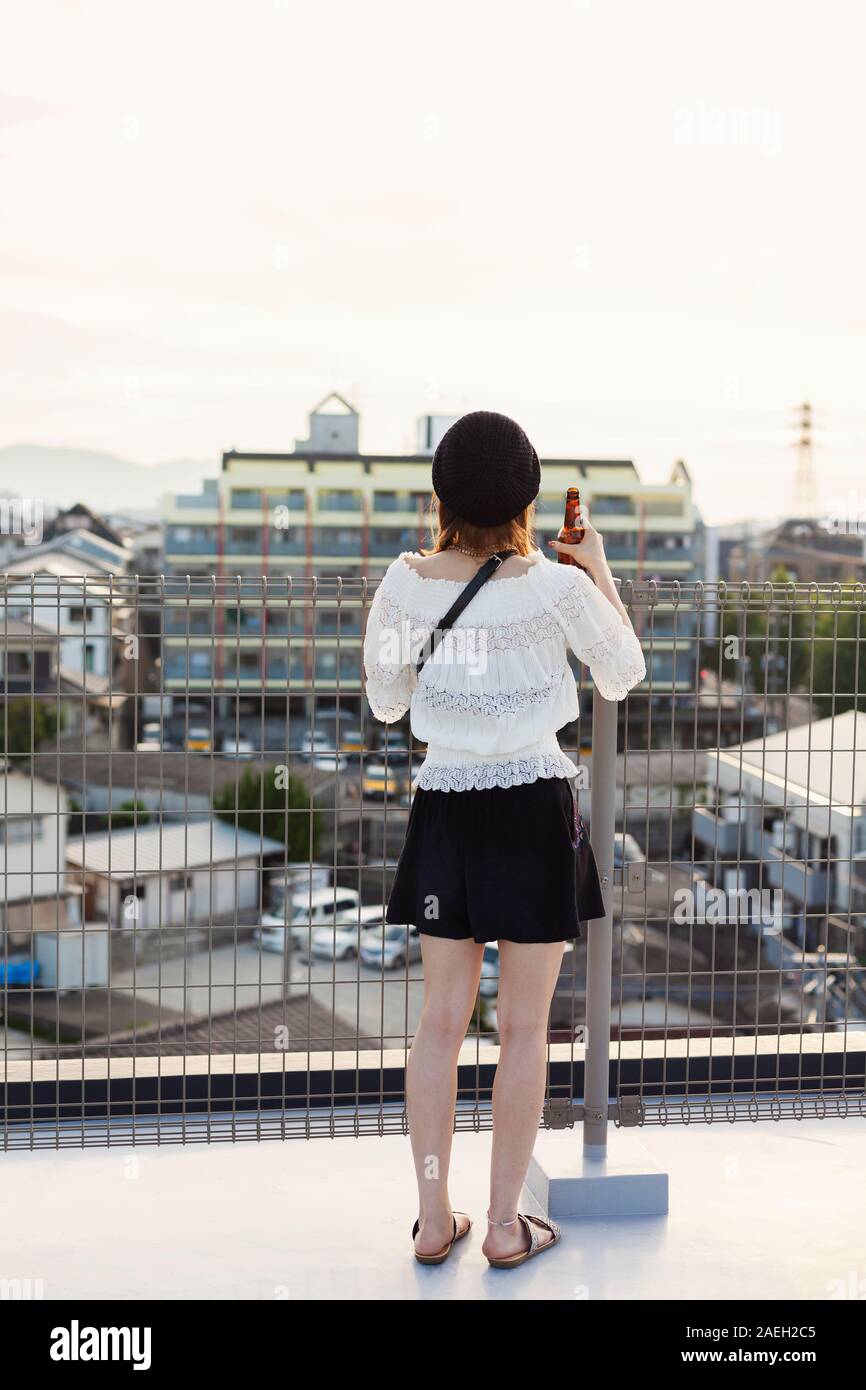 Rear view of young Japanese woman standing on a rooftop in an urban setting. Stock Photo