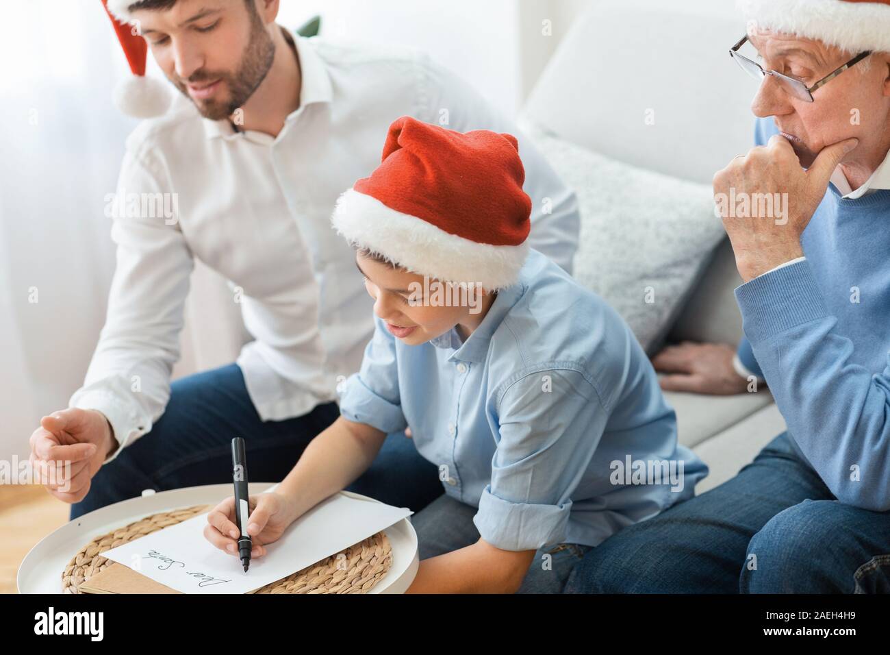 Boy Writing Christmas Wishlist Sitting With Father And Grandfather Indoor Stock Photo