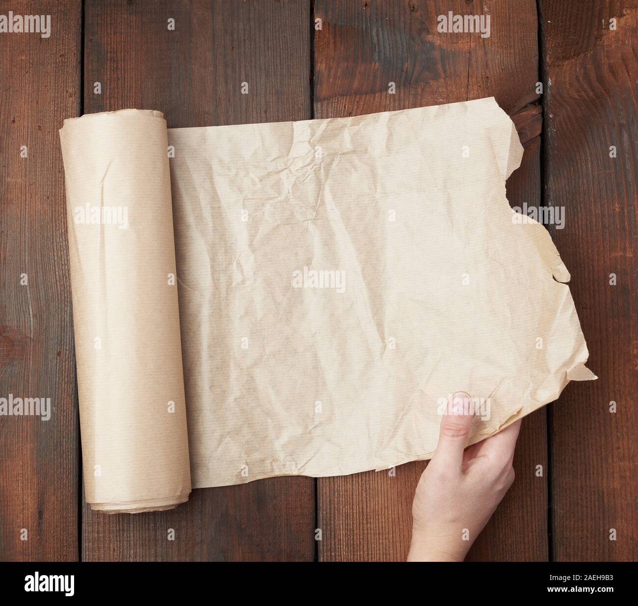 hand holds unfolded roll with brown parchment paper on wooden background, top view Stock Photo