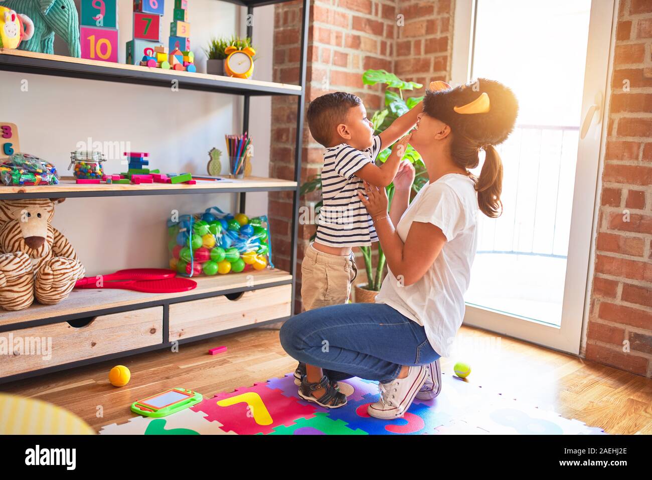 Beautiful teacher and toddler boy playing, woman with monkey mask at kindergarten Stock Photo