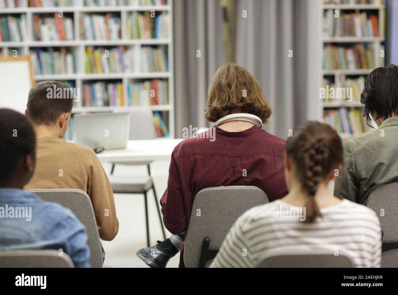 Rear view of group of young people sitting on chairs and working in the ...