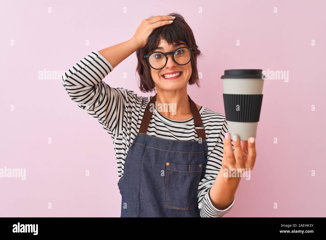 Young beautiful barista woman wearing glasses holding coffee over isolated pink background stressed with hand on head, shocked with shame and surprise Stock Photo