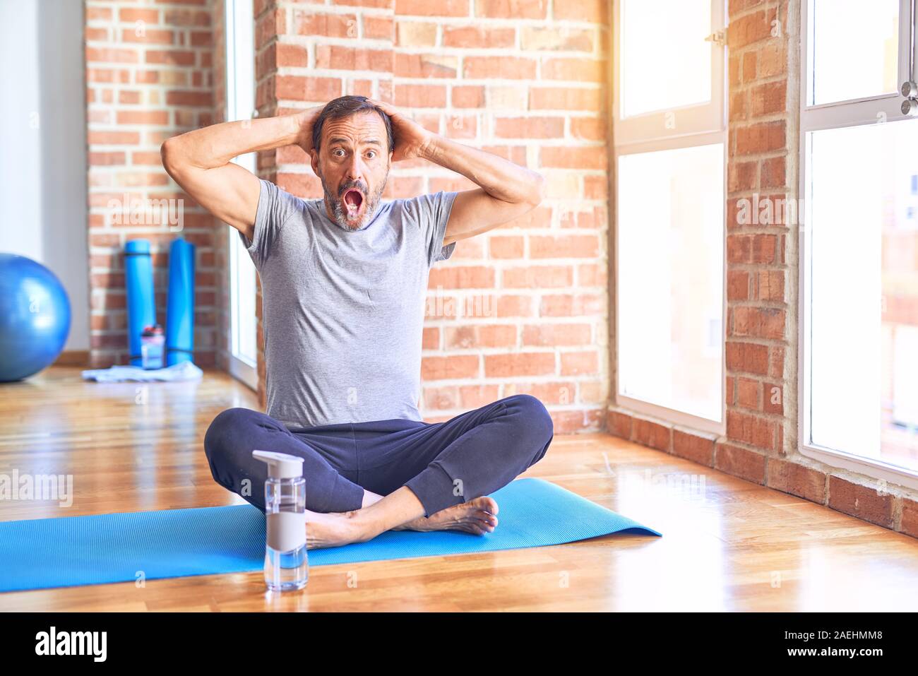 Middle age handsome sportman sitting on mat doing stretching yoga exercise  at gym Crazy and scared with hands on head, afraid and surprised of shock w  Stock Photo - Alamy