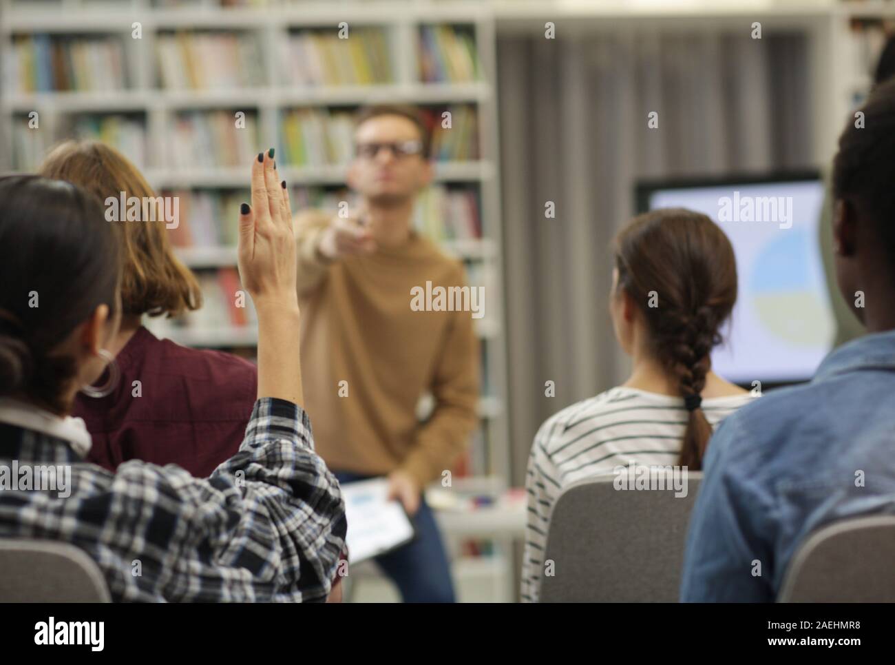 Rear view of young woman raised her hand she is going to ask the