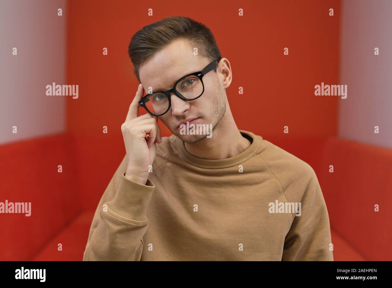 Portrait of young man in eyeglasses looking at camera and thinking about something Stock Photo