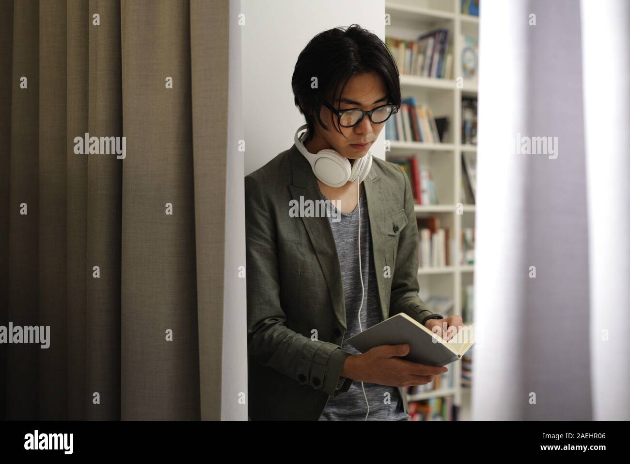 Young Asian man in eyeglasses standing in the library and he is fond of reading books Stock Photo