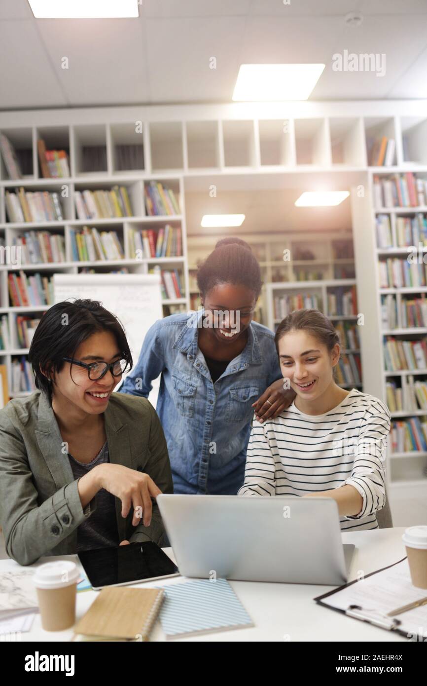Group of young people laughing while watching online presentation on laptop at the table in the library Stock Photo