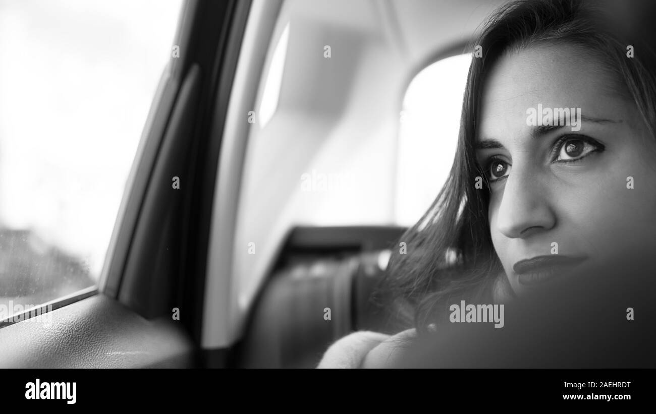 Monochromatic portrait of beautiful Happy Woman that Rides on a Passenger Back Seat of a Car, Looks out of the Window in Wonder. Big City View Reflect Stock Photo