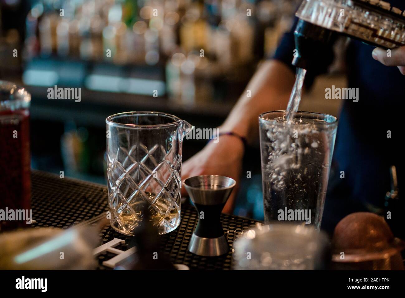 A bartender uses a soda dispenser to pour soda into a glass at a bar Stock Photo