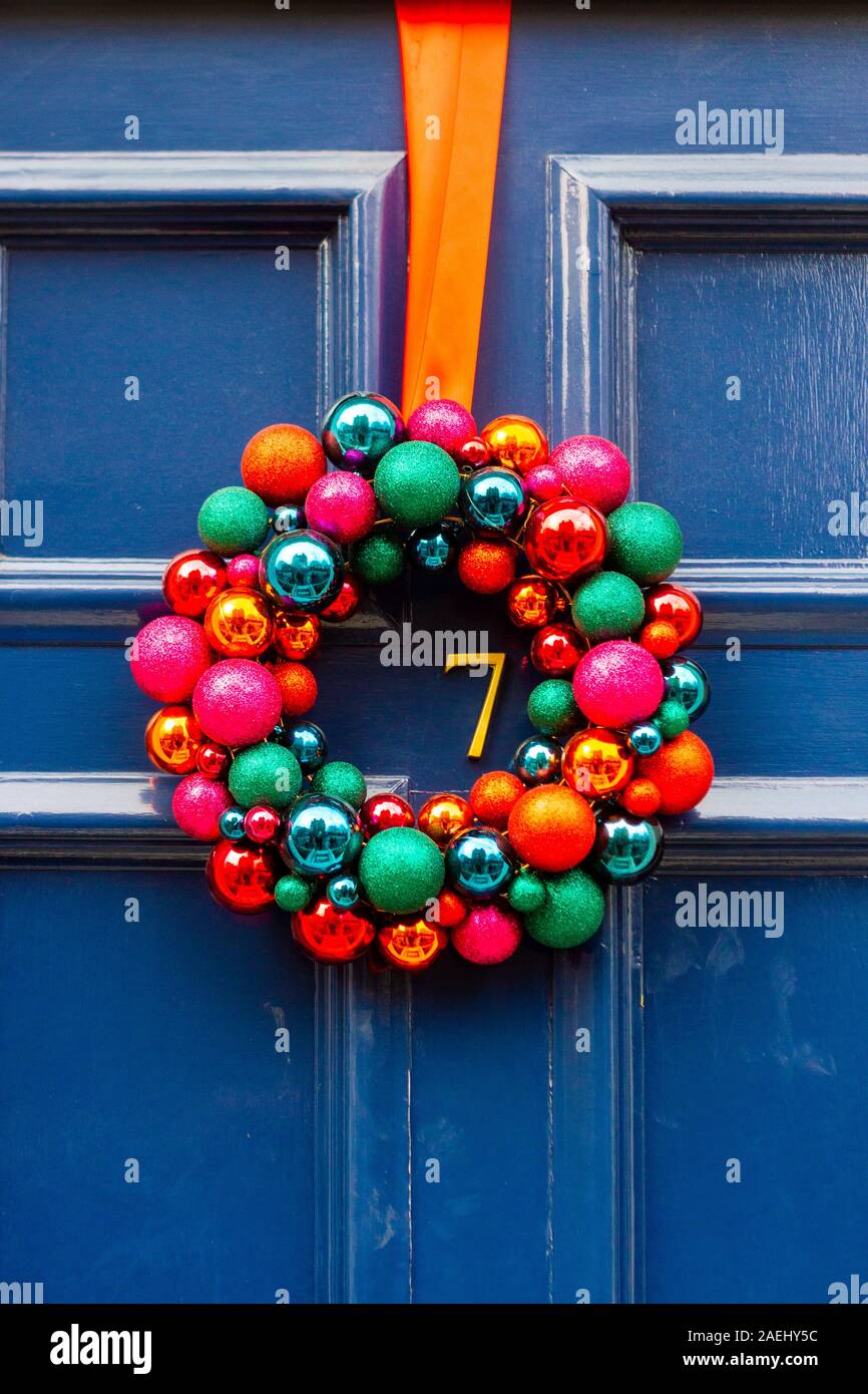 Colorful Christmas wreath made out of bright balls hanging on blue wooden front door with the house number 7 Stock Photo