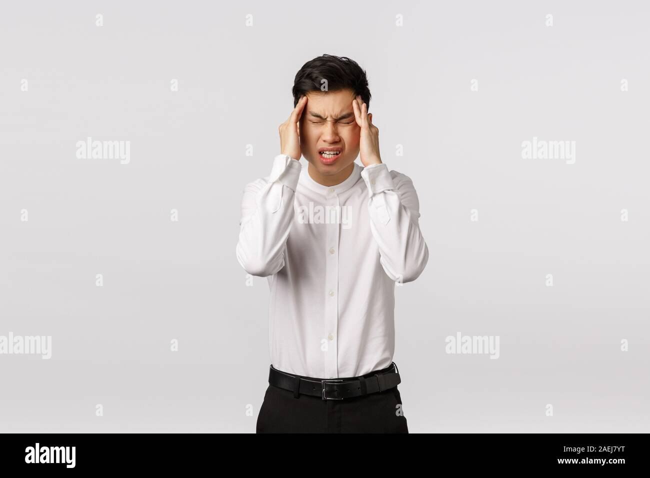 Come on need think. Tensed and distressed asian young man suffering big headache, close eyes, frowning and grimacing from pain, rubbing temples, have Stock Photo