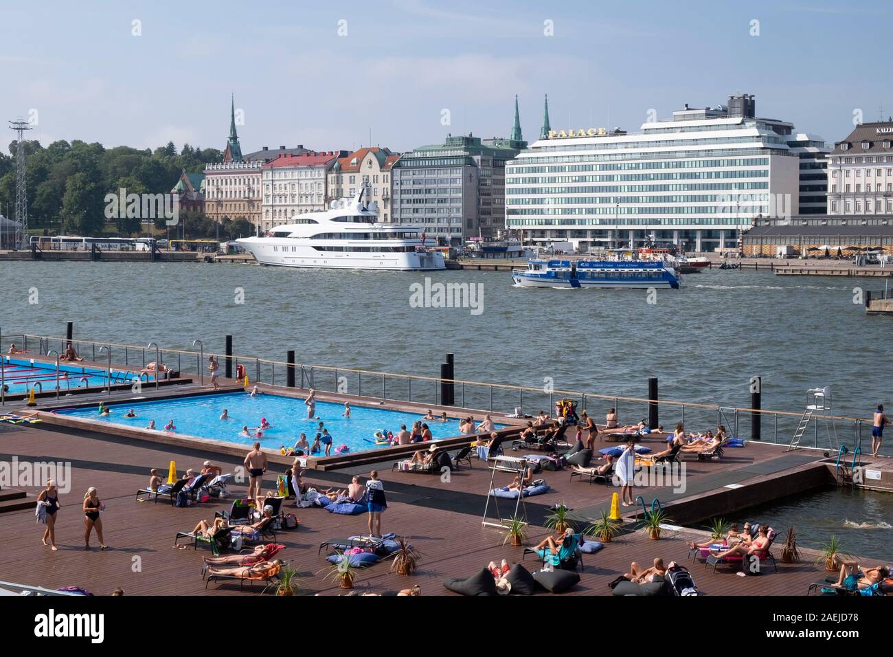 People sunbathing at Allas Sea Pool with big yacht and Hotel Palace in ...