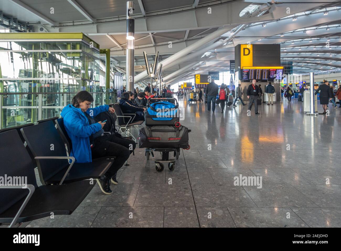 A view of the check in hall at Terminal 5, Heathrow Airport, London, UK. People sit and wait on benches. Stock Photo