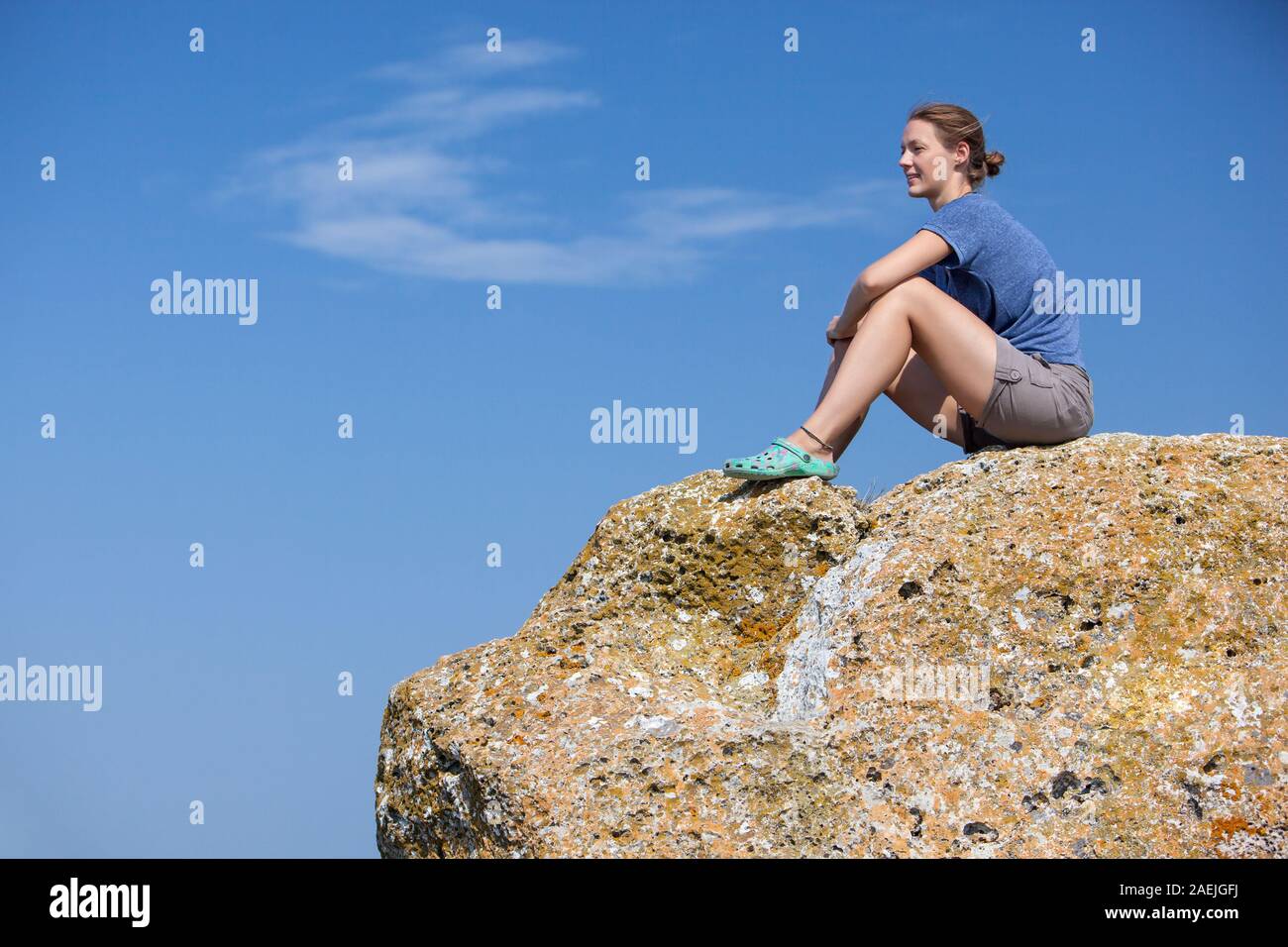 Woman traveler sitting near sea on top of cliff in summer mountains and enjoying view of sea and nature. Stock Photo