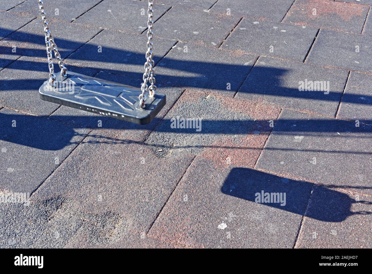 Empty swing casting shadows on the tiled ground. Stock Photo