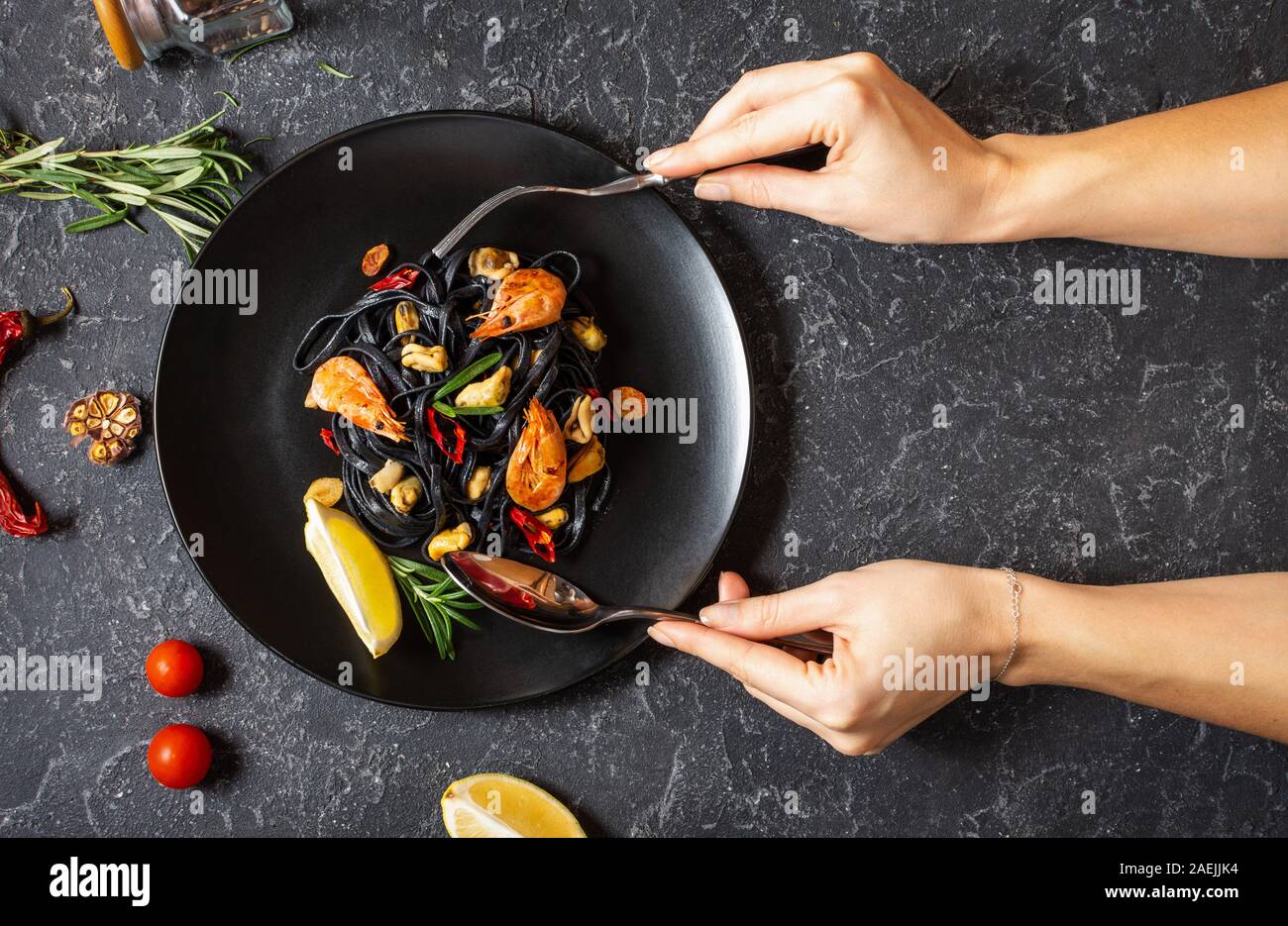 Female hands holds spoon and fork. Black spaghetti. Seafood pasta with