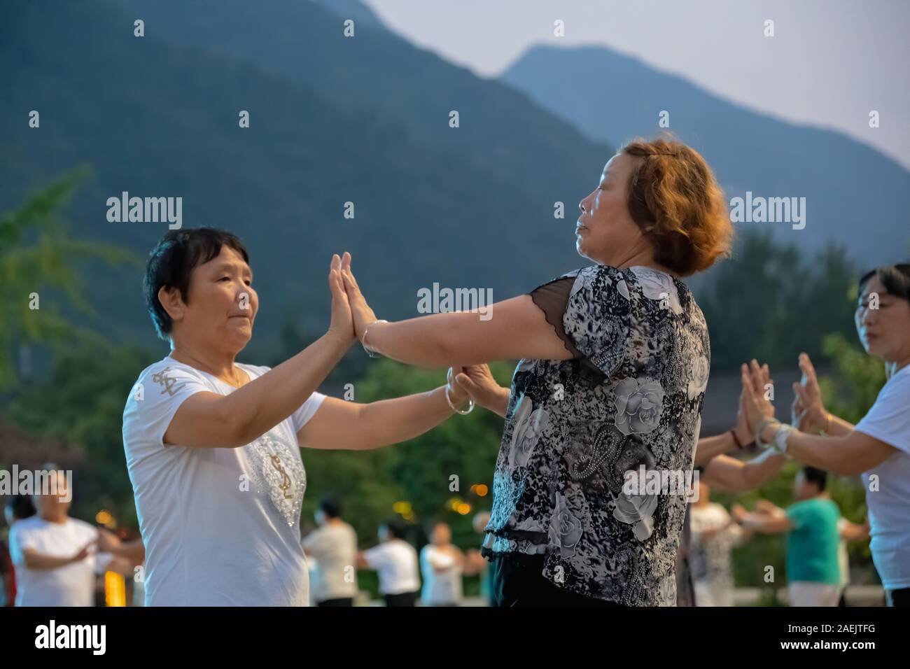 Huashan, China -  August 2019 : Group of Chinese women dancing in the open plaza square at the foot of HuaShan mountain at dusk, Shaanxi Province Stock Photo