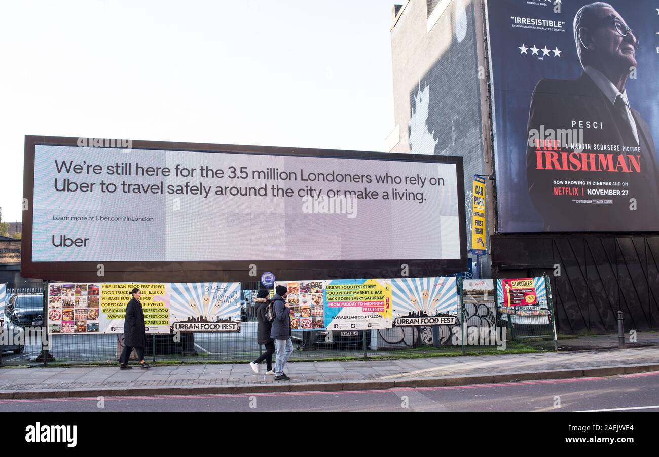 Big digital billboard in Shoreditch High Street advertising for the tech transportation company Uber next to traditional billboard promoting The Irish Stock Photo