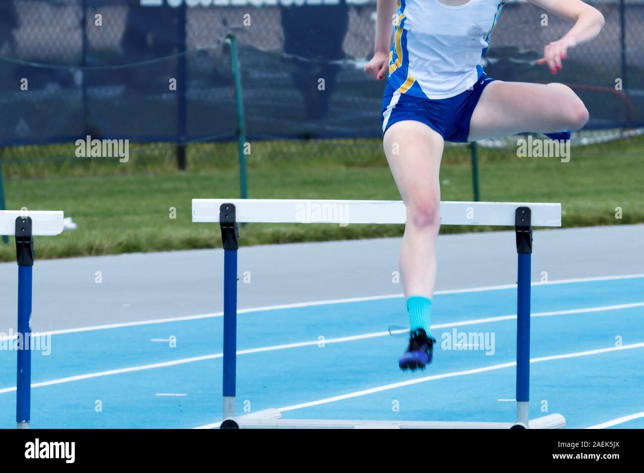 High school girl is racing the 400 meter hurdles on a blue track