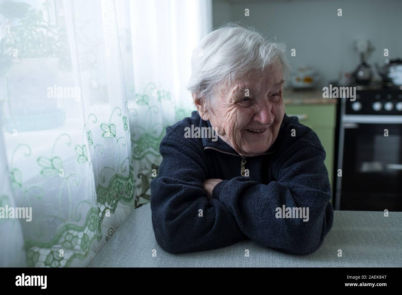 Old woman laughs sitting at the table. Elderly and pensioners. Stock Photo