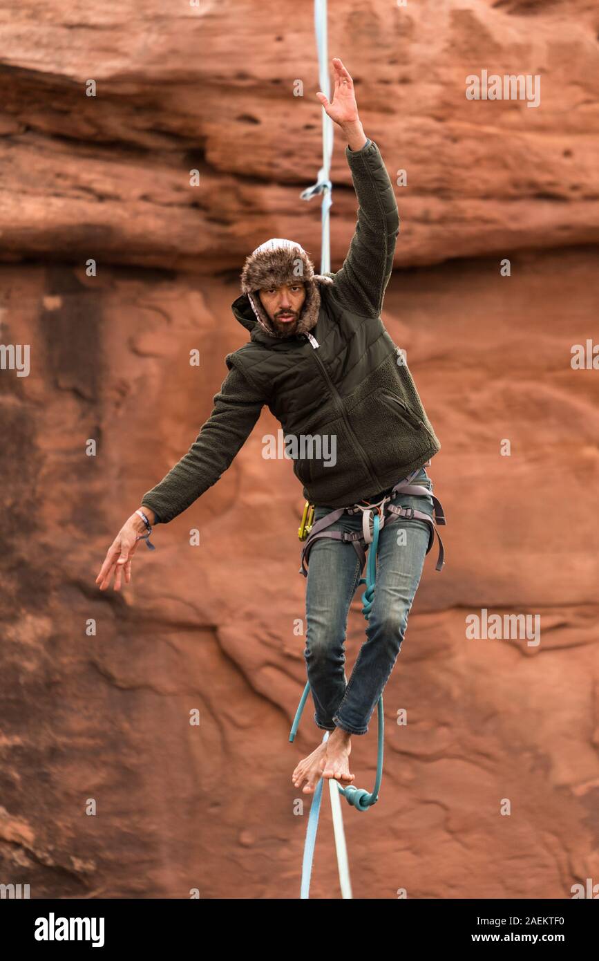 A young man slacklining or highlining struggles to maintain balance hundreds of feet above Mineral Canyon near Moab, Utah during a highline gathering. Stock Photo