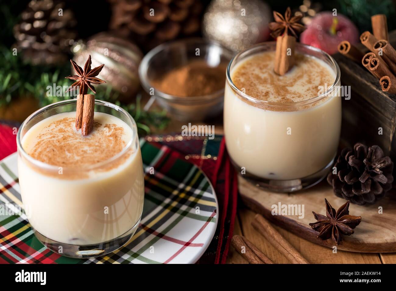 A close up view of two glasses of egg nog with cinnamon and star anise and surrounded by Christmas decorations. Stock Photo