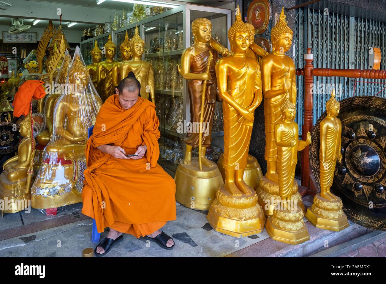 A Buddhist monk sits between Buddha statues at a shop for Buddhist