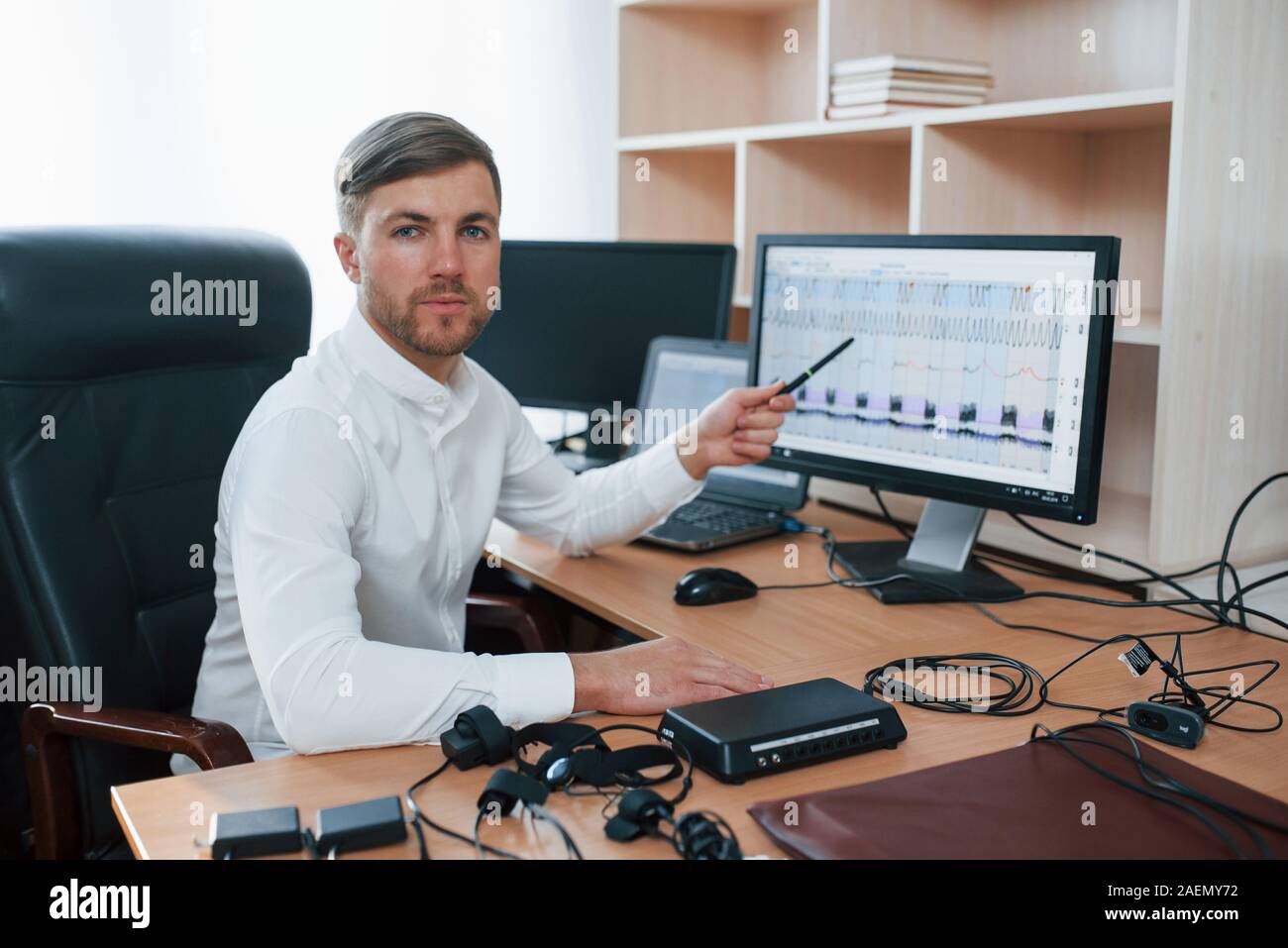 Looking into the camera. Polygraph examiner works in the office with his lie detector's