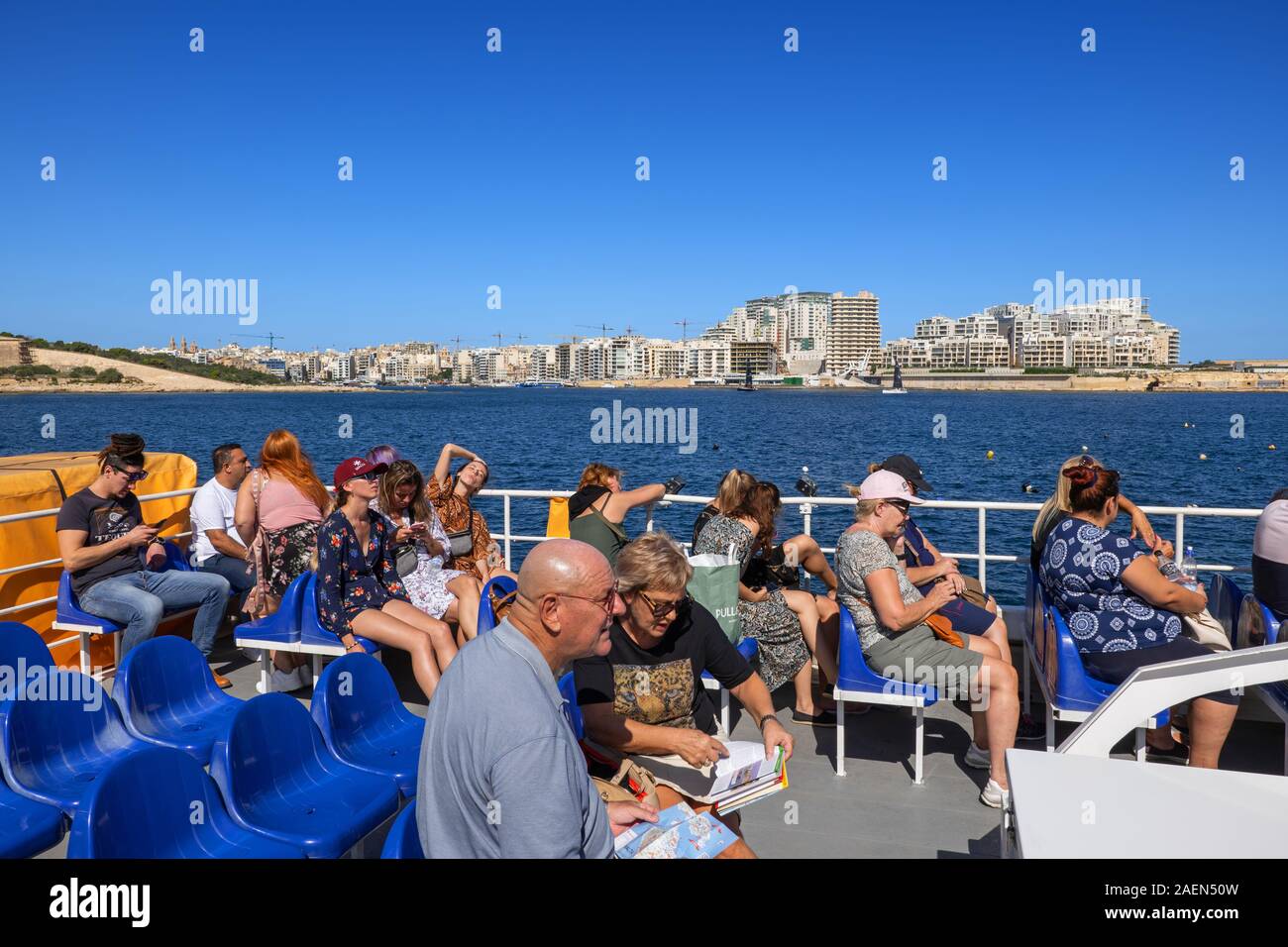 Valletta, Malta - October 17, 2019: Valleta Ferry Services boat with group of people, tourists on the top deck with Sliema skyline at Marsamxett Harbo Stock Photo