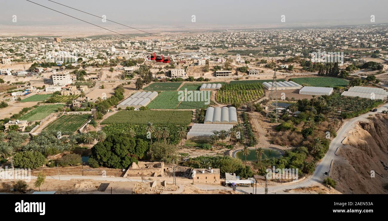 red cable cars going up to the mount of the temptation of jesus in jericho with modern high tech farms in the foreground and the palestinian city in t Stock Photo