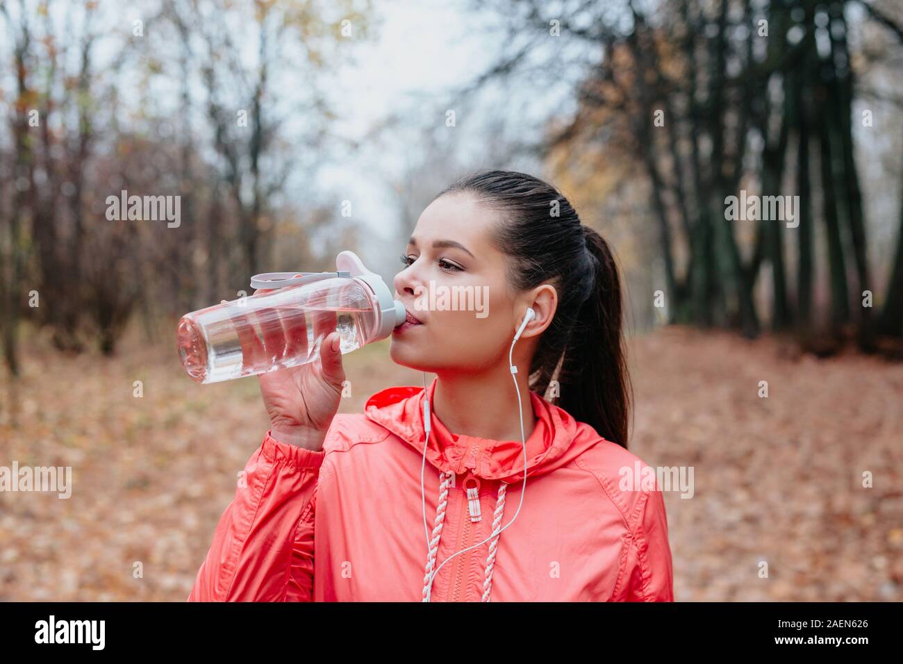 Young sports woman drinking fresh water from the bottle in the autumn park . Sport lifestyle. Stock Photo