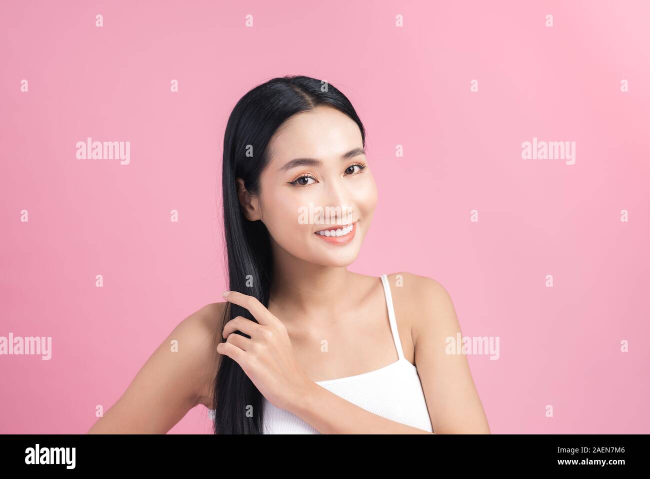 Young beautiful Asian woman taking care of her hair. Beauty portrait , natural make-up, beauty face, isolated over pink background. Stock Photo