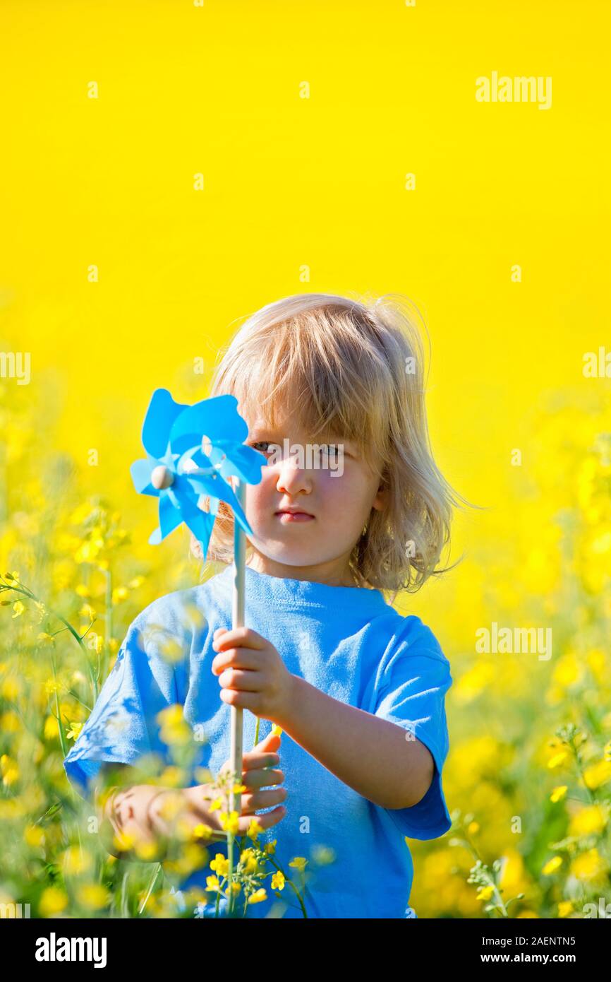 boy with long blond hair holding pinwheel in canola field Stock Photo