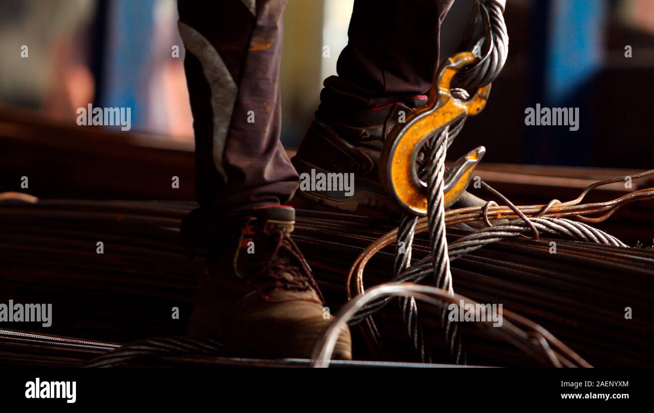 Worker loading rebar and hanging the load on the crane's chains in metalworking factory. Concept for industrial worker, manual work and manufacturing. Stock Photo