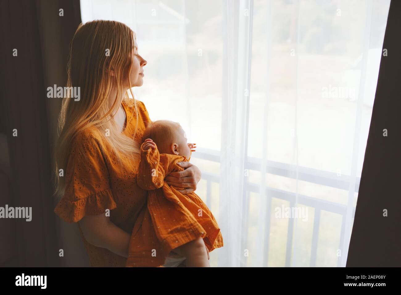 Mother and daughter baby at home family lifestyle mom and child together looking out window maternity concept Mothers day holiday dress clothing Stock Photo