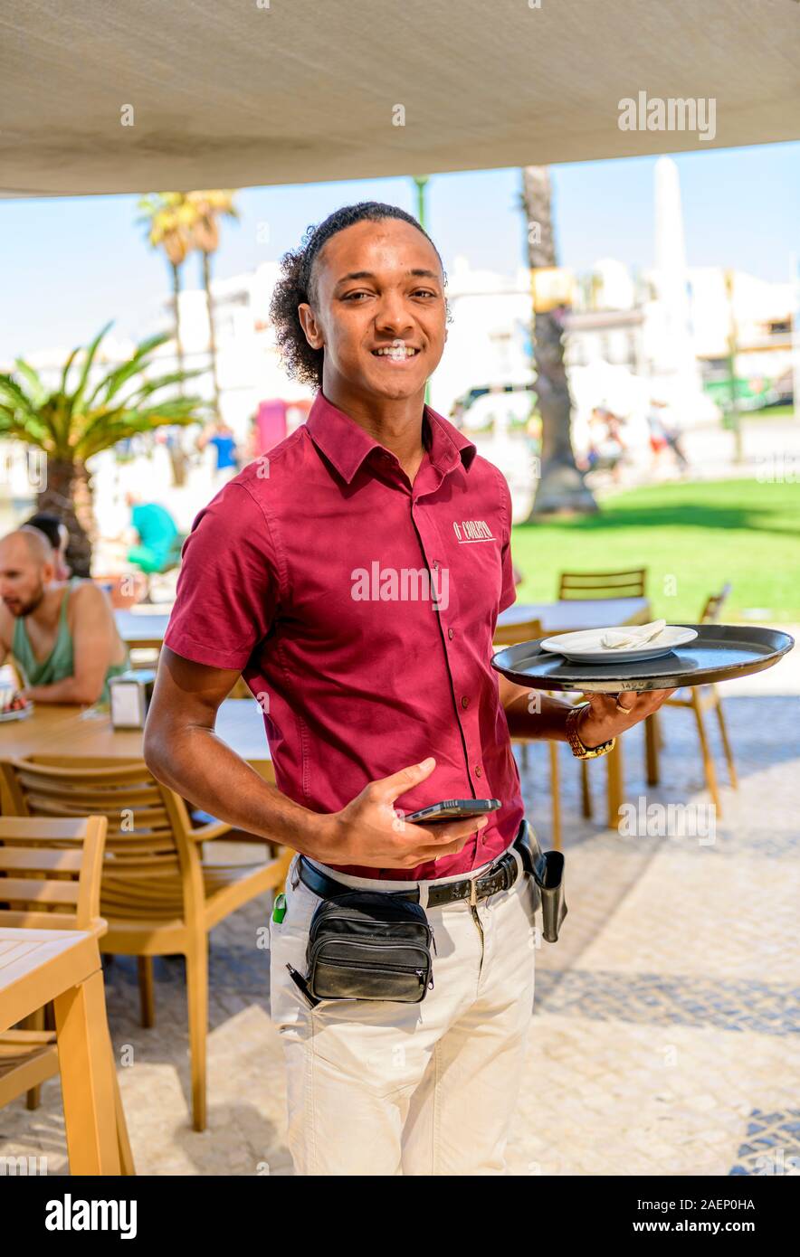 Young ethnic Faro waiter serving at a pizza restaurant. Faro, East Algarve Portugal, Stock Photo