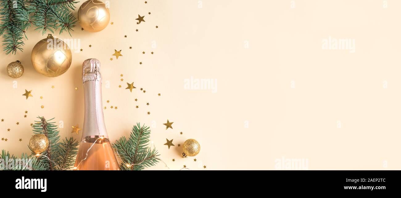 Christmas Celebration Background. Champagne bottle with golden star cofetti and fir branches on beige pastel background. Holiday, party and celebratio Stock Photo