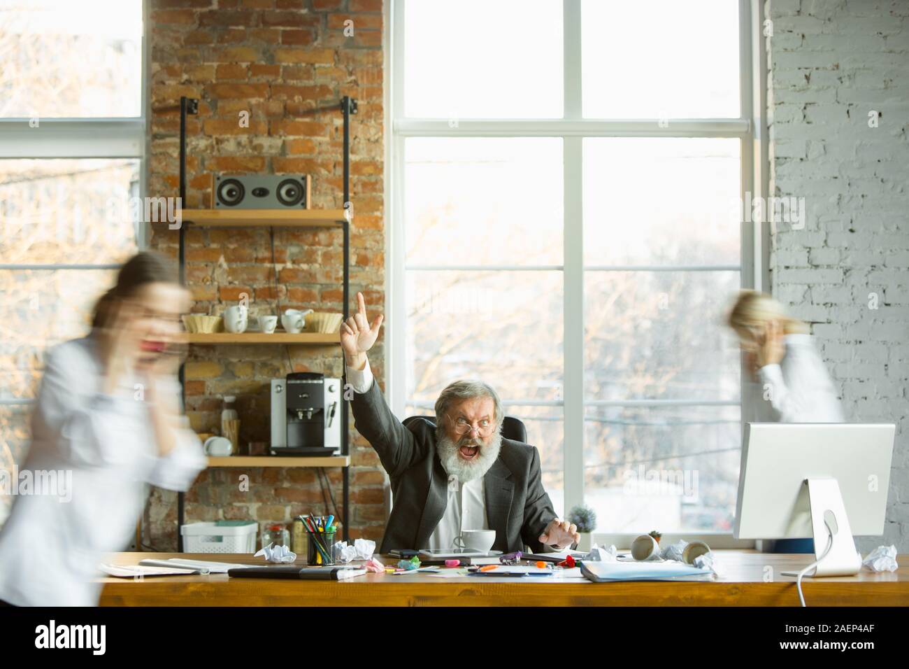Tired boss resting at his workplace while busy people moving near blurred. Office worker, manager working, drinking coffee and giving directions for his colleagues. Business, work, workload concept. Stock Photo