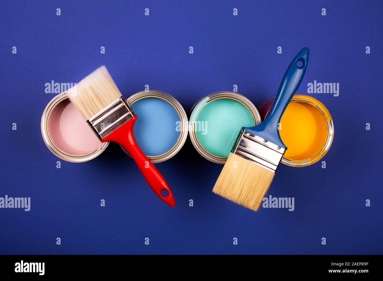 Four open cans of paint with brushes on blue background. Yellow, blue