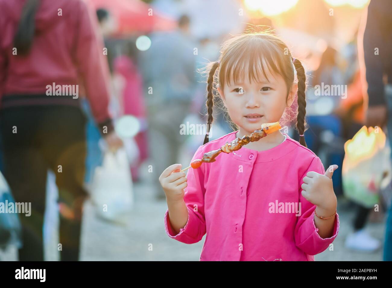 Little asian girl walking on street of Bangkok, buy barbeque and eating street food in evening time Stock Photo
