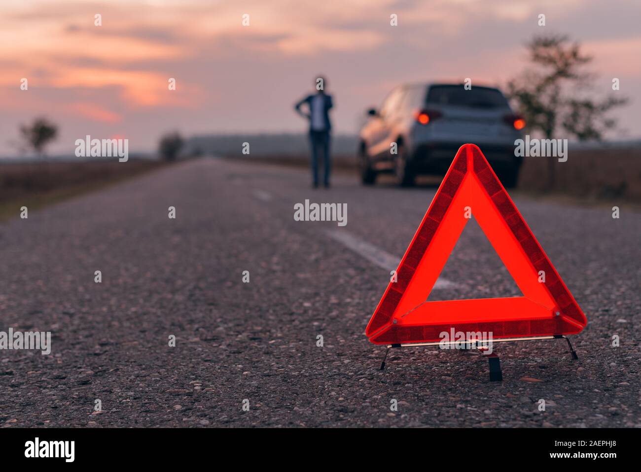 Warning triangle sign on the road, woman in blur background calling for roadside assistance by the broken car, selective focus Stock Photo