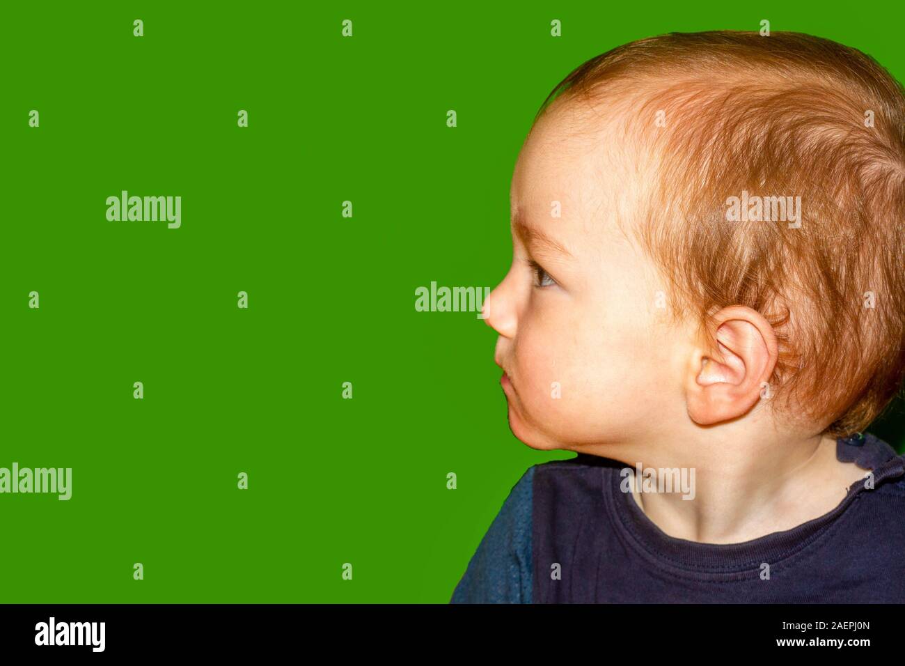 Little boy staring critically to the side seen in profile in front of a green background Stock Photo