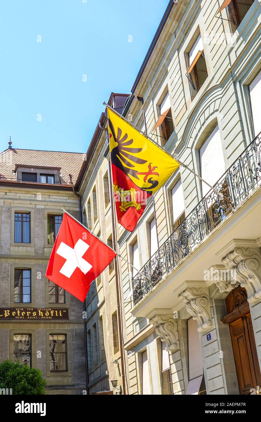 Geneva, Switzerland - July 19, 2019: Old town buildings in the city center with waving Swiss flag and the flag of Geneva. Facades of the historic houses. Vertical photo. Stock Photo