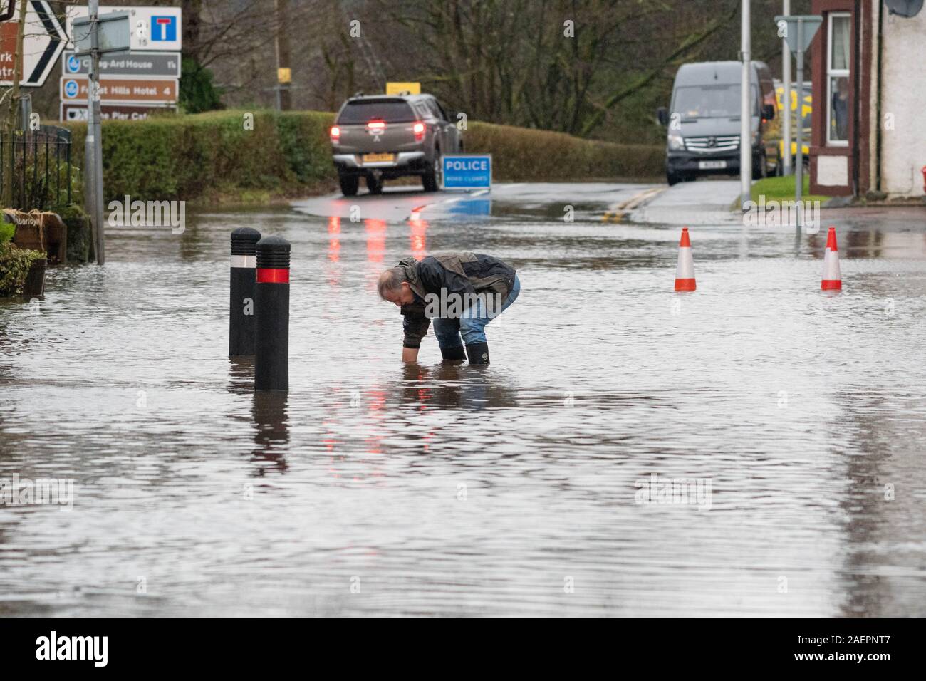 Aberfoyle, Stirlingshire, Scotland, UK. 10th Dec, 2019. UK weather - a men keeps a drain clear on the main street in Aberfoyle during a day of heavy flooding after the River Forth bursts its banks Credit: Kay Roxby/Alamy Live News Stock Photo