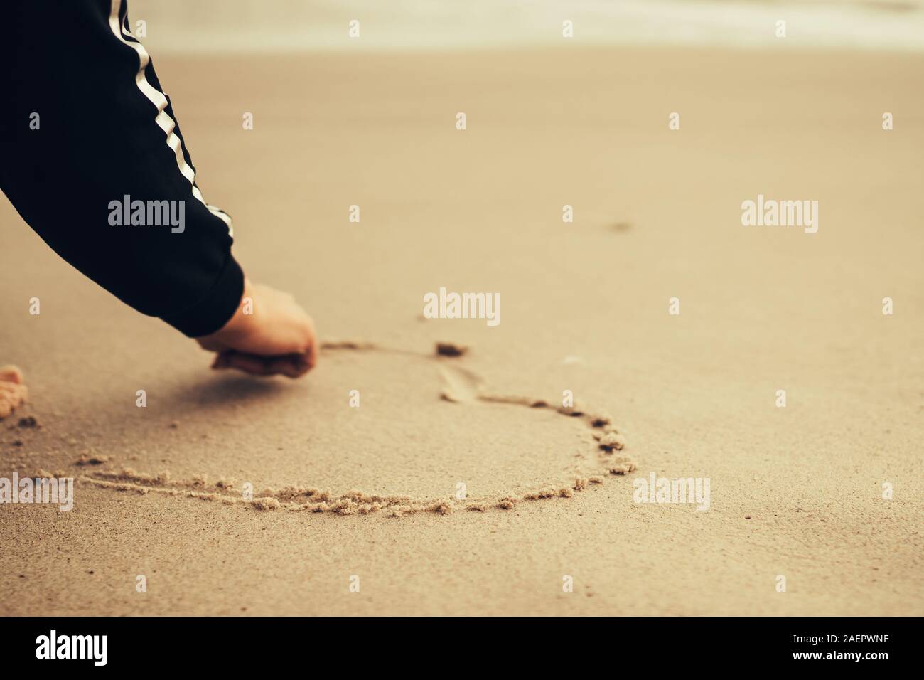 Girl at the beach drawing hearts on a sand.  love concept. Selective focus Stock Photo