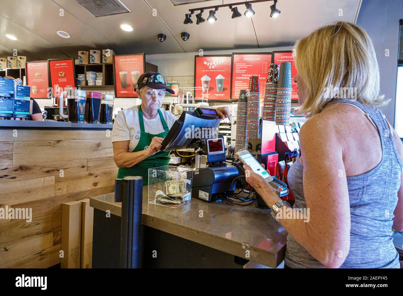 Palm Beach Gardens Florida,Starbucks Coffee,cafe,coffeehouse,inside interior,counter,senior,woman,working,barista,customer,ordering,mobile,smartphone, Stock Photo