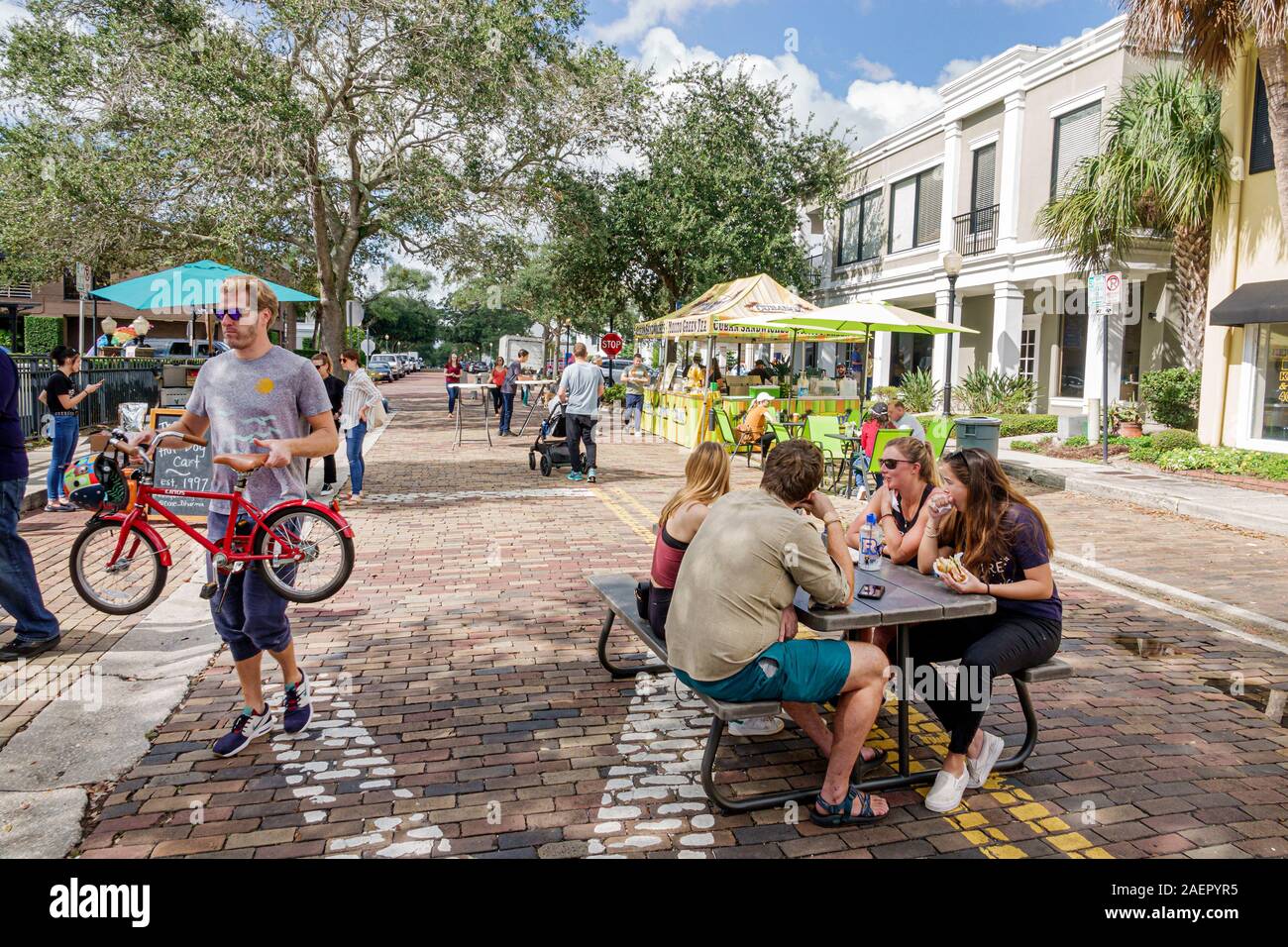 Orlando Winter Park Florida,Downtown,historic district,Farmers' Market,weekly Saturday outdoor,closed road,picnic table,man,woman,carrying child's bic Stock Photo